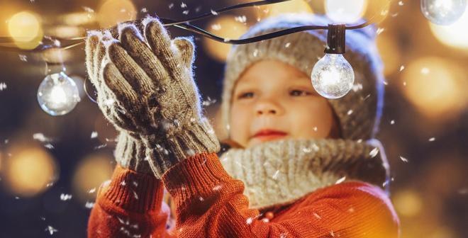 child in snow holding a festive lightbulb